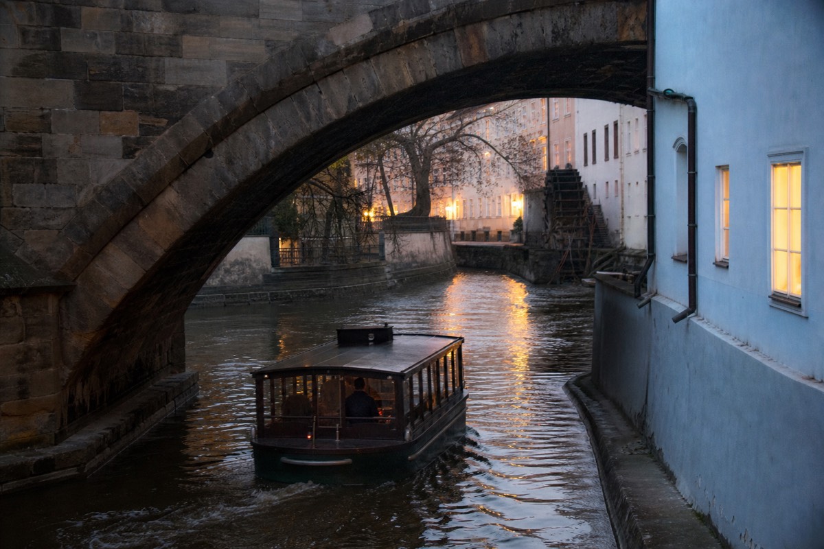 Small boat gliding under an arch of Charles Bridge into the Čertovka canal