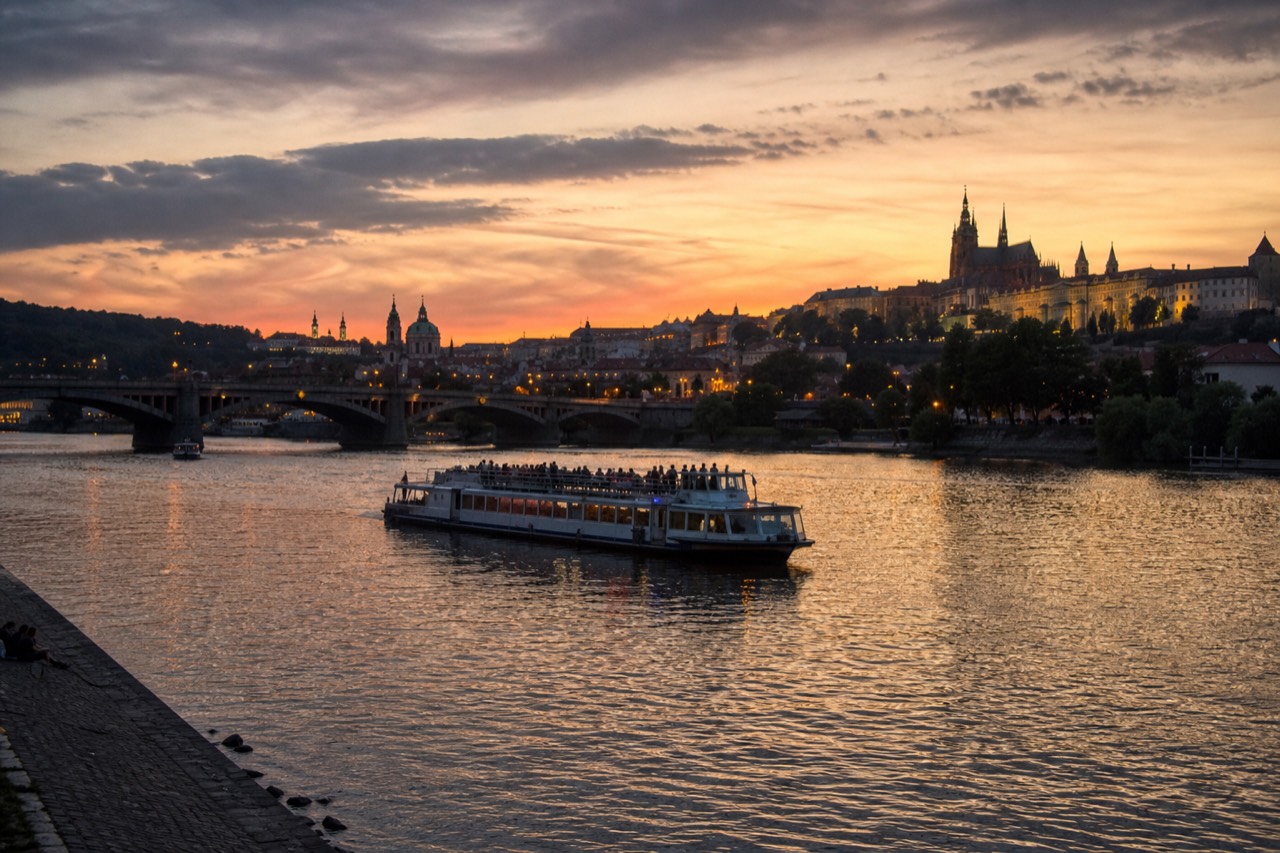 Open-top glass sightseeing boat on the Vltava passing the floodlit Charles Bridge and Prague Castle at dusk