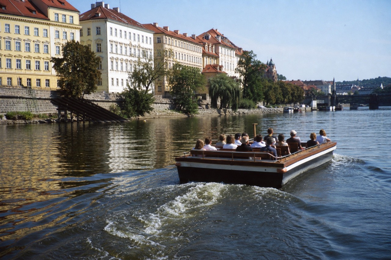 Several different Vltava tour boats on the river in Prague, an open-top glass boat, a small canal boat and a historic vessel, with Charles Bridge behind