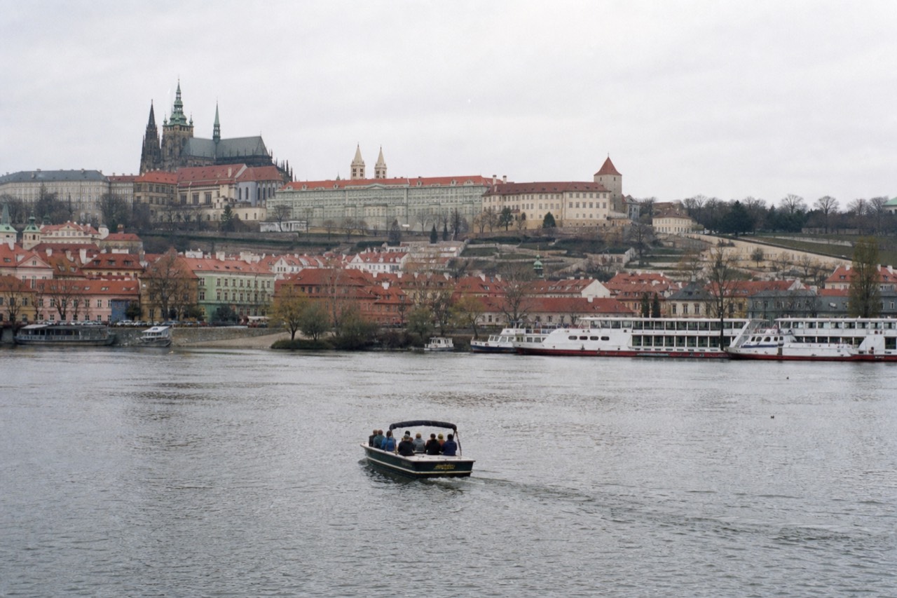 Small open-top sightseeing boat on the Vltava in central Prague below the castle, contrasted with the idea of a large multi-day river-cruise ship, no branding visible