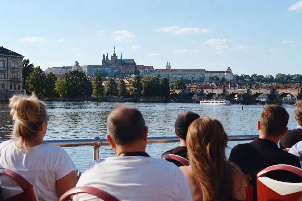 Open-top glass sightseeing boat on the Vltava in daylight passing Prague Castle and the National Theatre embankment