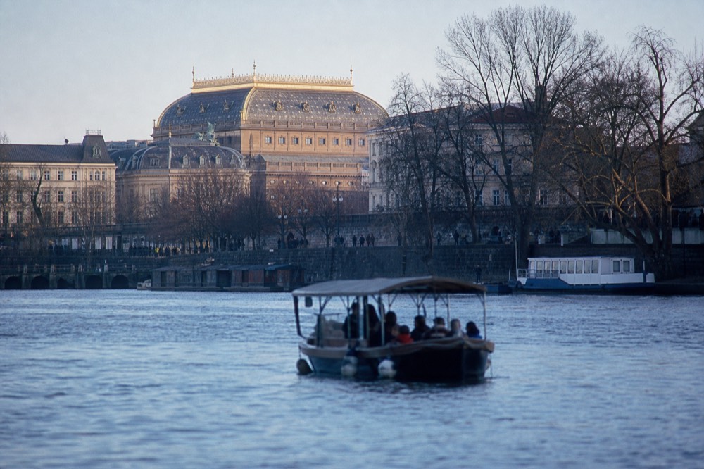 The National Theatre's gold-flecked roof seen from the river in late afternoon light, riverside trees framing it