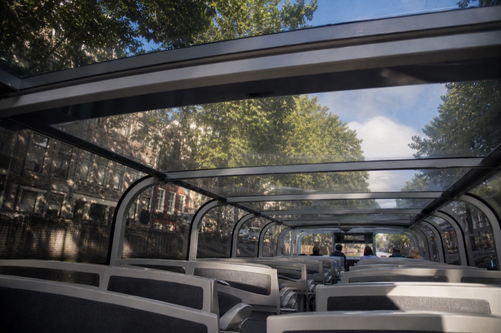 The interior of an empty open-top glass cruise boat, rows of seats catching daylight through the glass roof