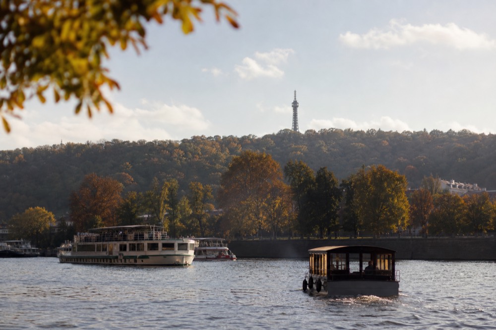Petřín hill's wooded slope and distant lookout tower behind the river, soft hazy afternoon light