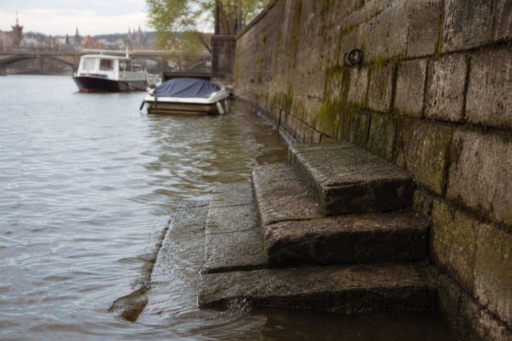 Old worn stone steps and a mossy quay wall descending into the Vltava, ripples lapping the lowest step, texture and age in the stonework